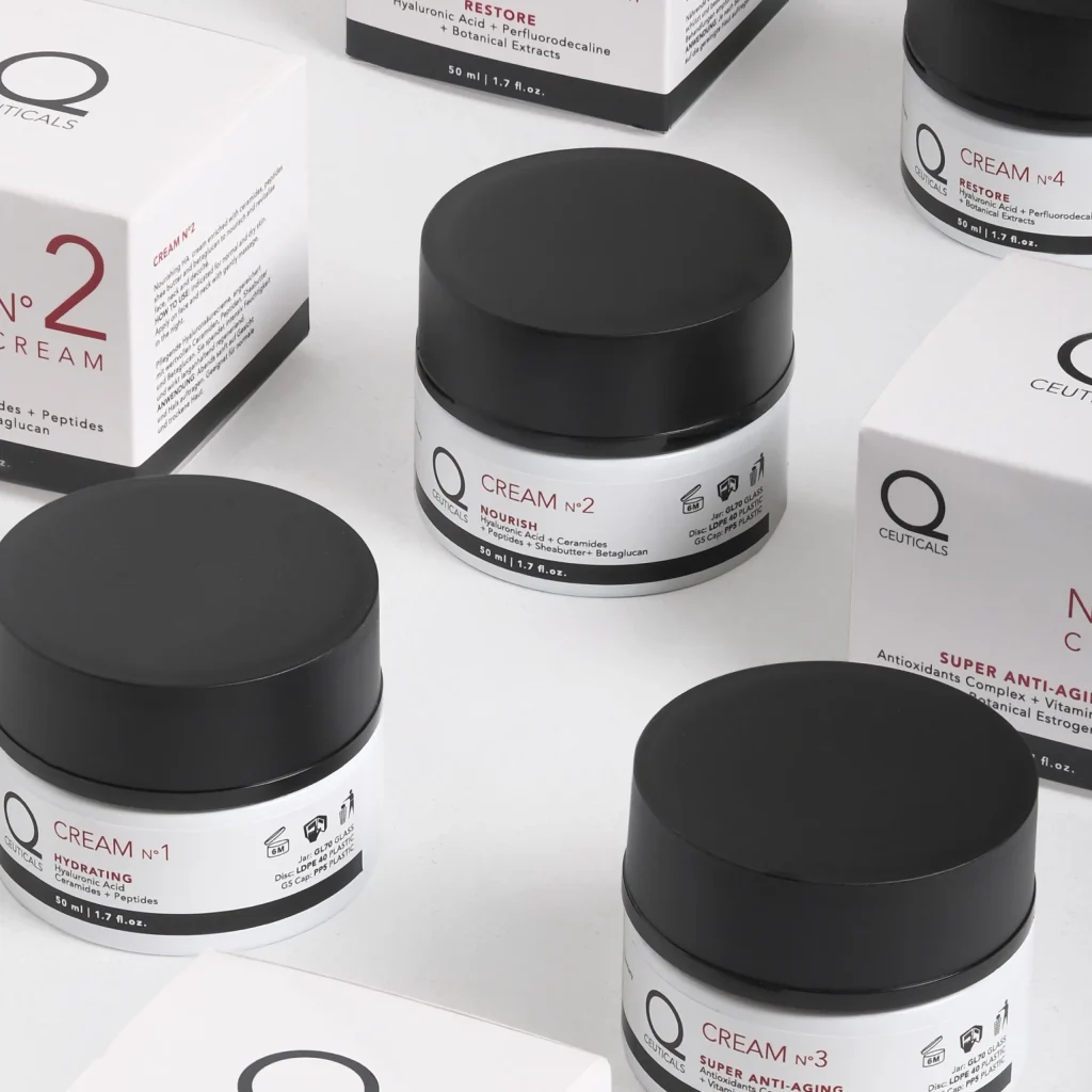 Various jars and boxes of Q Cream skincare products are displayed on a light background. The image highlights an assortment of numbered creams and serums, each adorned with product details and branding. With a minimalist design, the collection features black lids paired with white containers, epitomizing elegant cosmetics from the company Q Cream.